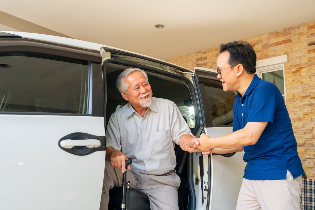 Caregiver helping senior patient into a vehicle for medical transportation