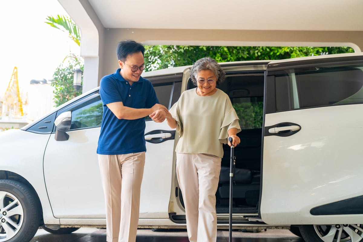 Driver helping senior woman patient get in the car for medical transportation