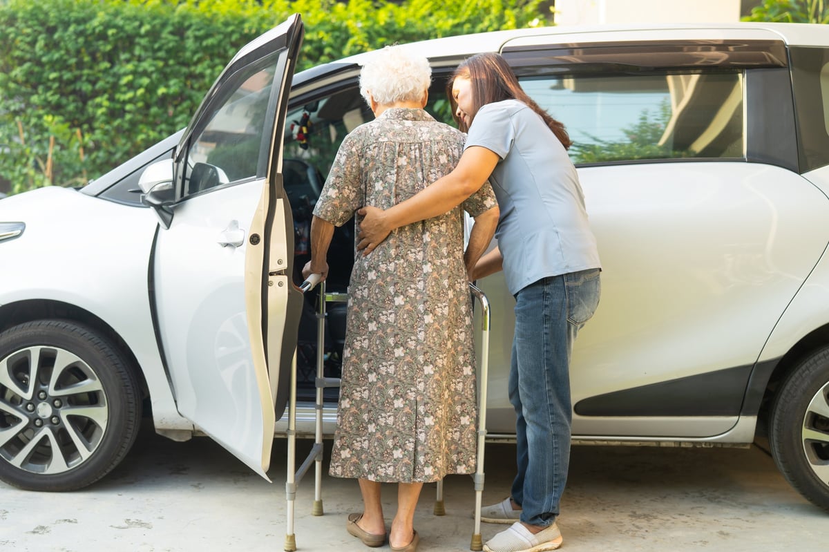 Driver helping elderly woman patient get into car